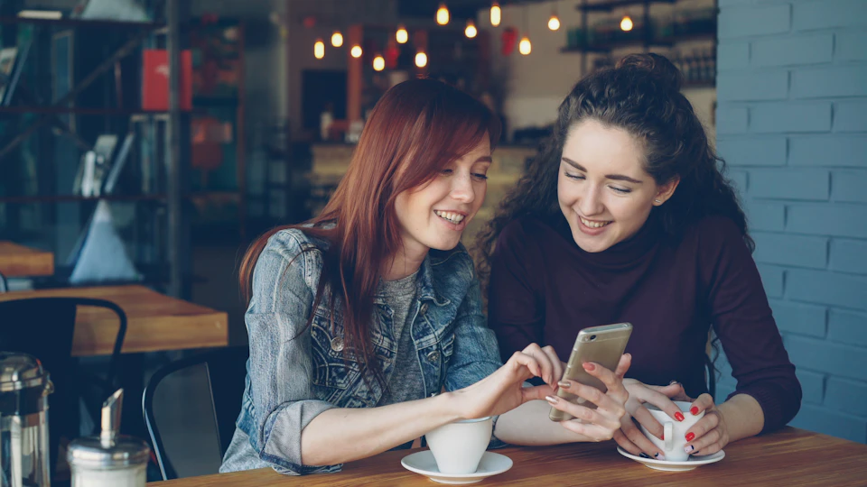 Two women looking together at a smartphone in a cafe.